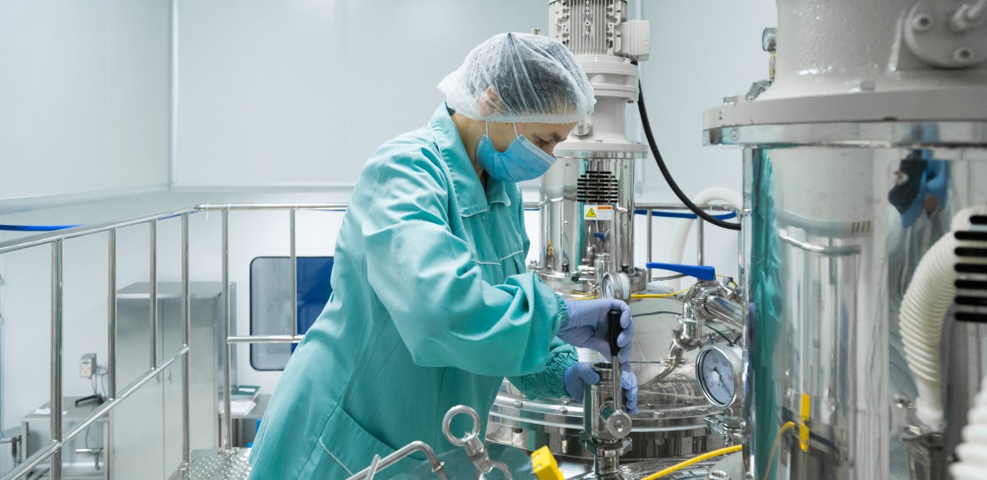 Pharmaceutical factory woman worker in protective clothing operating production line in sterile environment